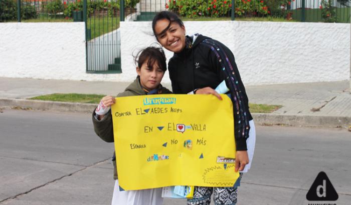 Niña y educadora con pancarta sobre aedes aegypti